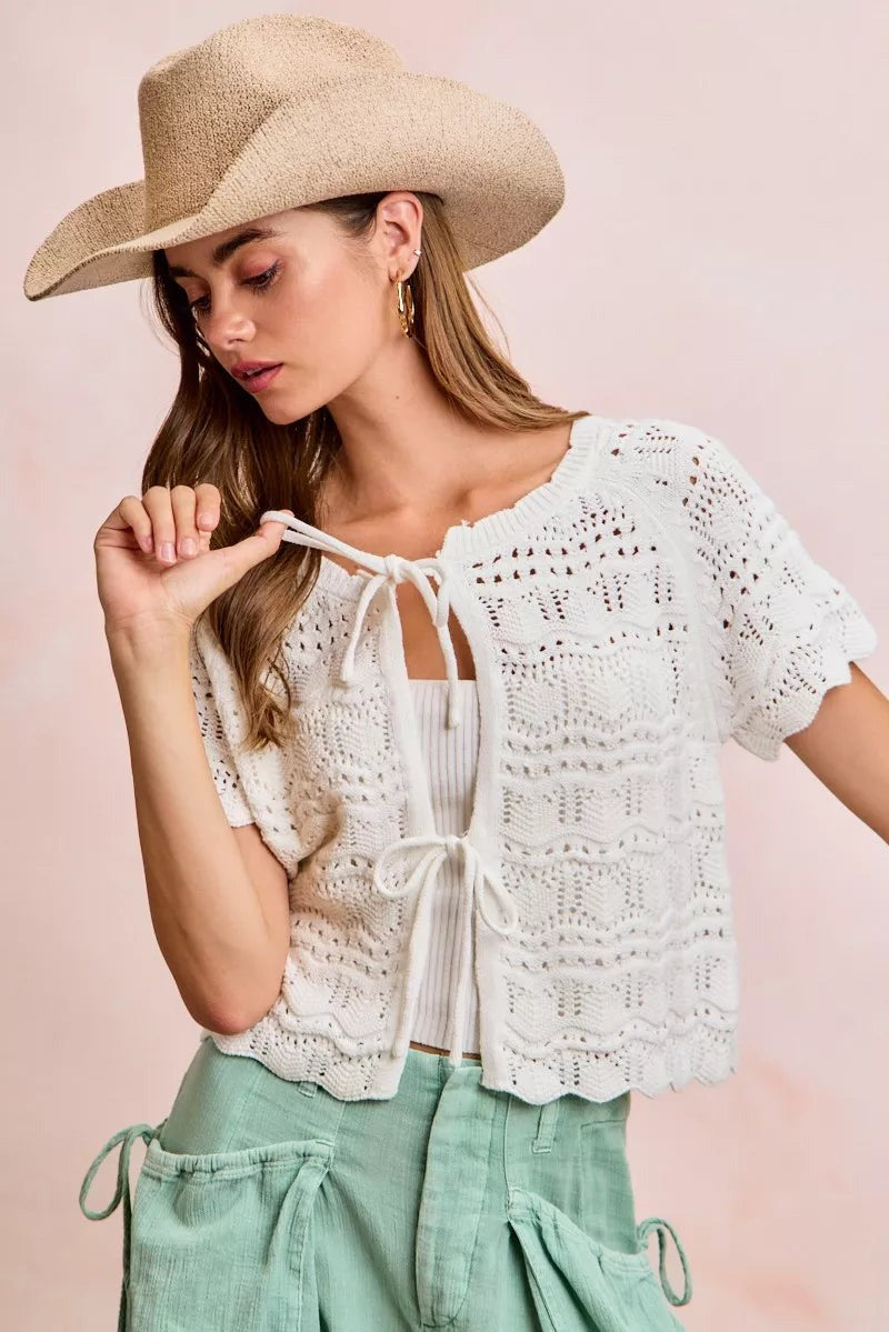 Model wearing a JUST-JEN BOUTIQUE ivory pointelle knit cardigan with short puff sleeves and front bow-tie closures.