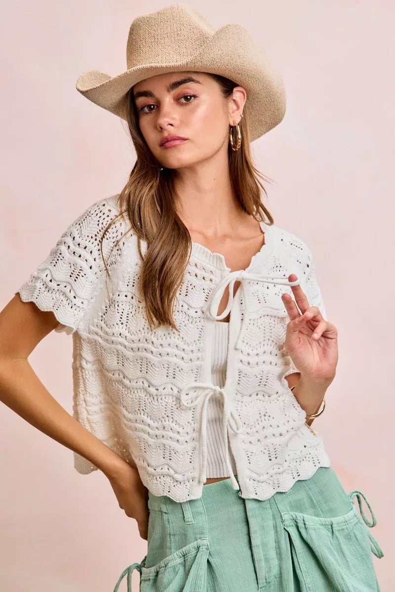 Model wearing a JUST-JEN BOUTIQUE ivory pointelle knit cardigan with bow-tie closures and a straw cowboy hat.