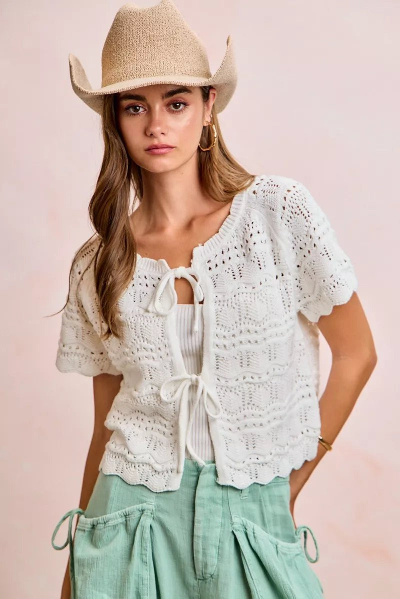 Model wearing a JUST-JEN BOUTIQUE ivory pointelle knit cardigan with bow-tie closures and short puff sleeves.