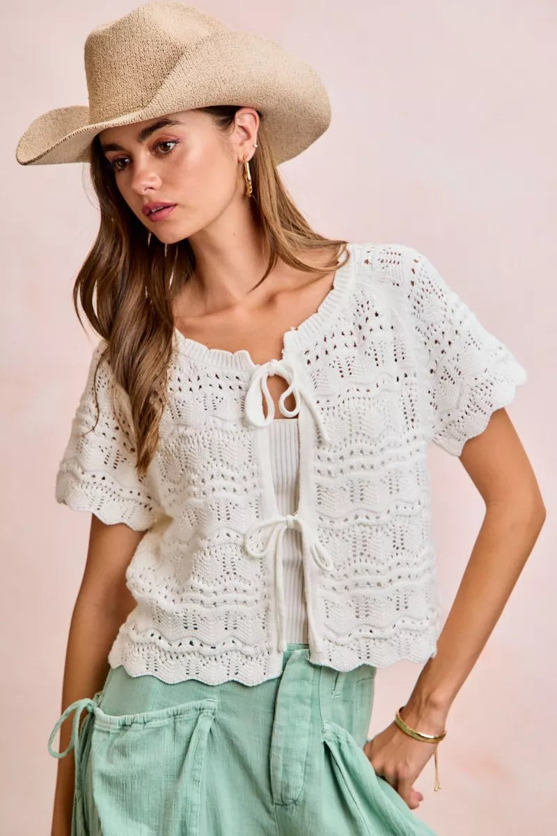 Model wearing a JUST-JEN BOUTIQUE ivory pointelle knit cardigan with short puff sleeves and bow-tie front closures.